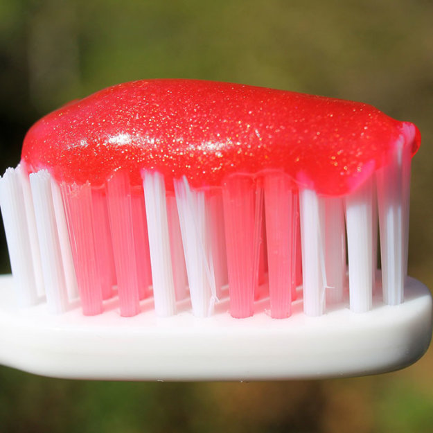 Toothbrush with red toothpaste blob on white bristles against blurred background.