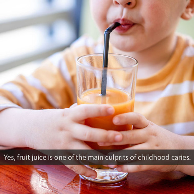 Child drinking fruit juice through straw from glass, illustrating childhood cavity risk factors.