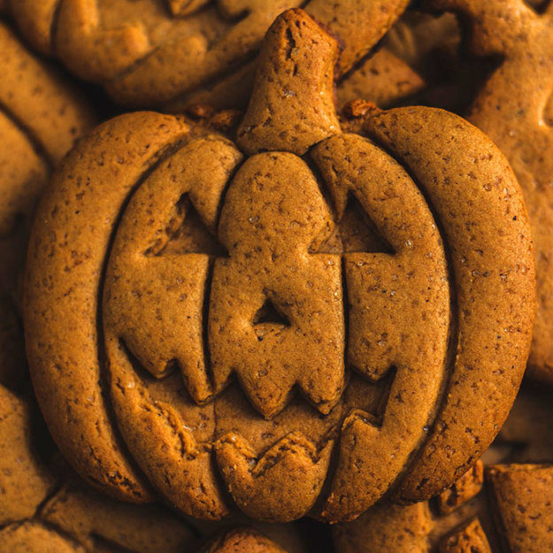 Pumpkin-shaped cookie with jack-o'-lantern face carved into it, surrounded by similar autumn-themed treats.