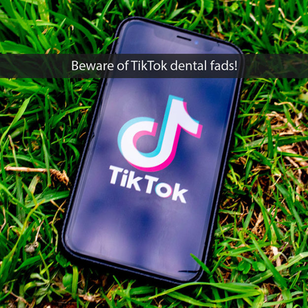 Smartphone displaying TikTok logo on grass with warning text about dental fads.