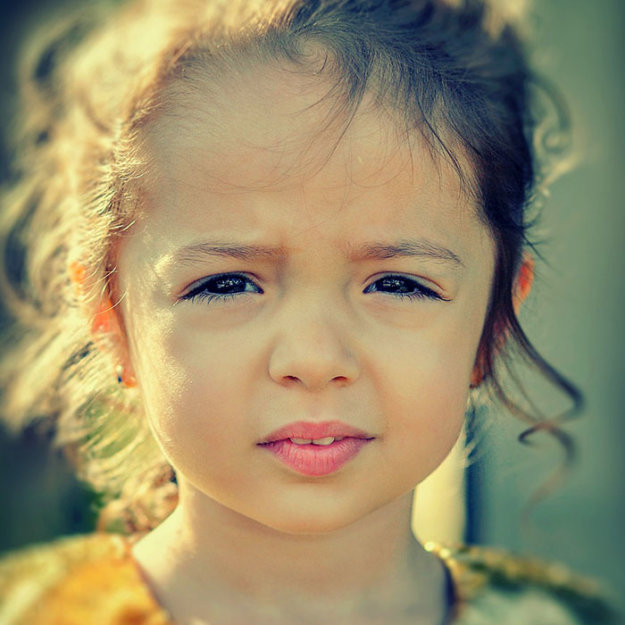 Young girl with blonde hair smiling at camera in outdoor portrait setting with natural lighting.