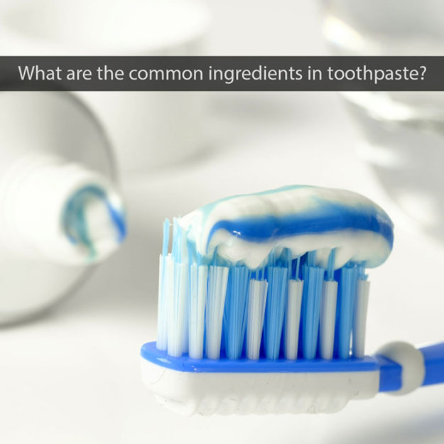Toothbrush with blue and white striped bristles displaying blue toothpaste in bathroom setting.