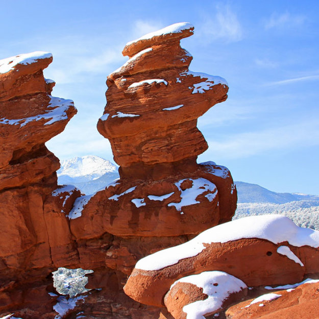 Red rock formations with snow patches under blue sky, desert landscape.