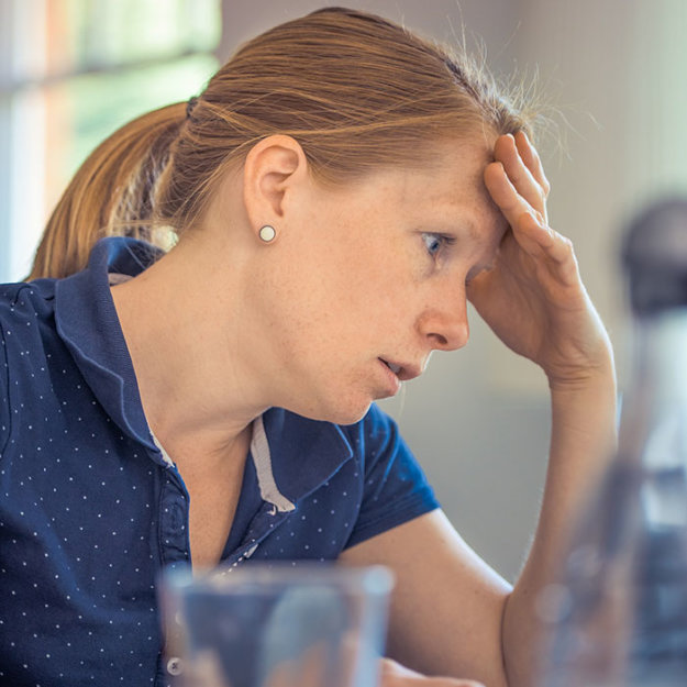 Woman in blue shirt with hand to head, appearing stressed or thoughtful in office setting.