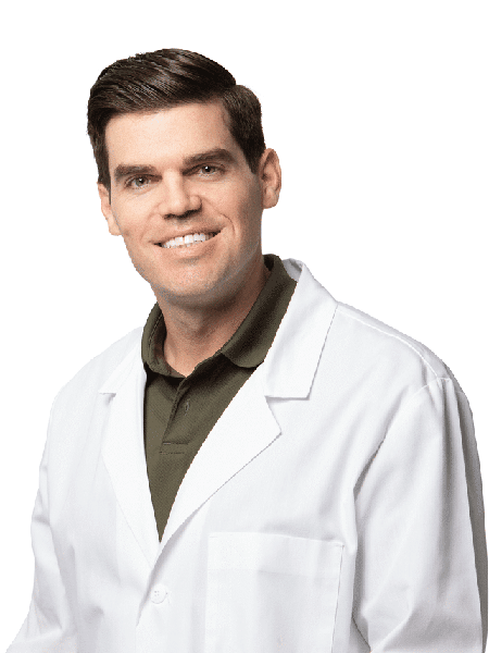 Male dentist wearing white lab coat smiling at camera in professional headshot.