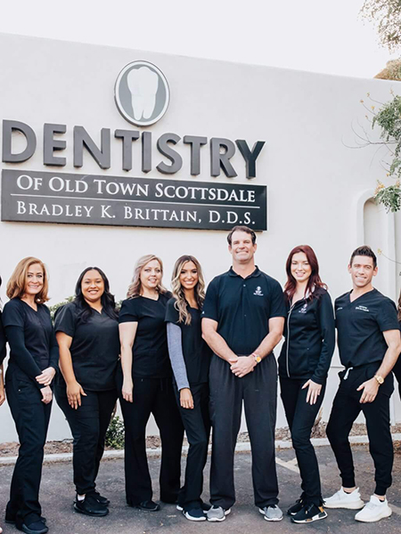 Dental team of nine professionals in dark uniforms standing in front of Dentistry of Old Town Scottsdale office sign.