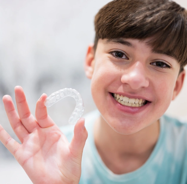 Smiling teenage boy holding a clear Invisalign aligner representing Invisalign for teens at Dentistry of Old Town Scottsdale