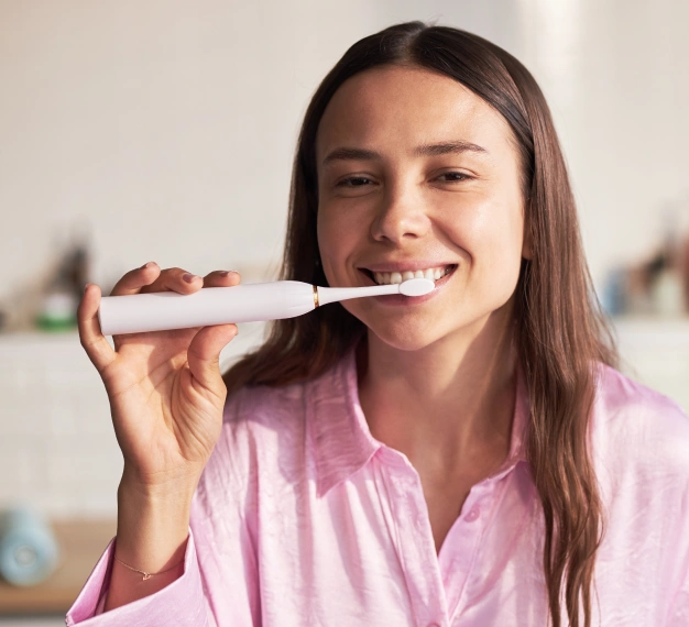 Smiling young woman brushing her teeth with a Philips Sonicare toothbrush representing oral hygiene recommendations in Scottsdale