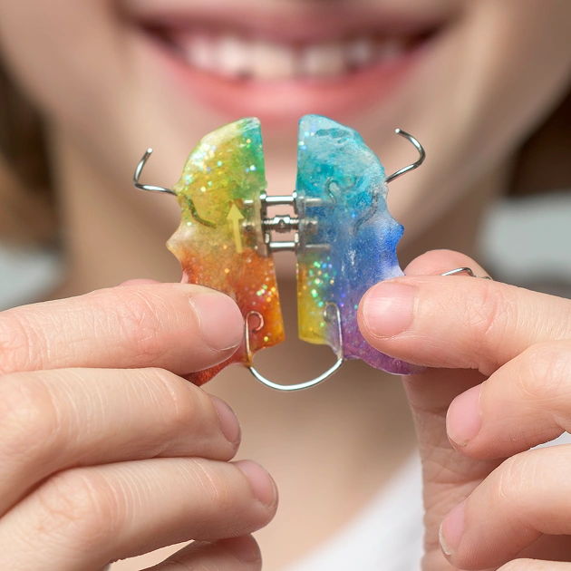 Close up of colorful orthodontic retainers being held representing why retention matters after orthodontic treatment