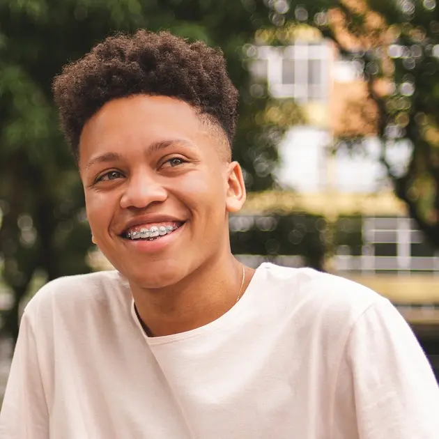 Smiling young man with braces wearing a light colored shirt outdoors.