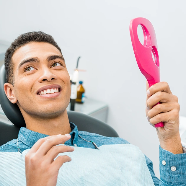 Smiling young man holding a pink mirror representing Rembrandt Sapphire teeth whitening in Scottsdale