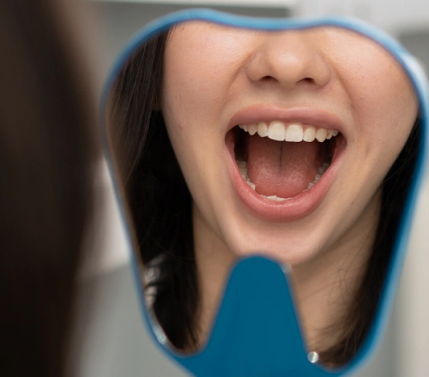 Patient viewing their oral cavity in a mirror before oral and maxillofacial surgery evaluation and treatment planning.